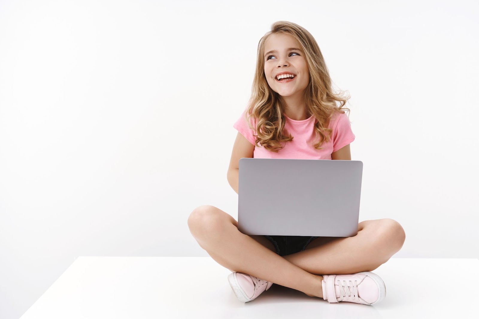 dziewczynka siedzi na podłodze z laptopem i rozwiązuje zagadki dla dzieci